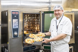 A PCH chef stands at an oven with a trayful of pizzas, ready to cook